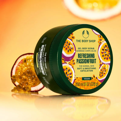 The Body Shop's Refreshing Passionfruit gel body scrub jar with a halved passionfruit beside it