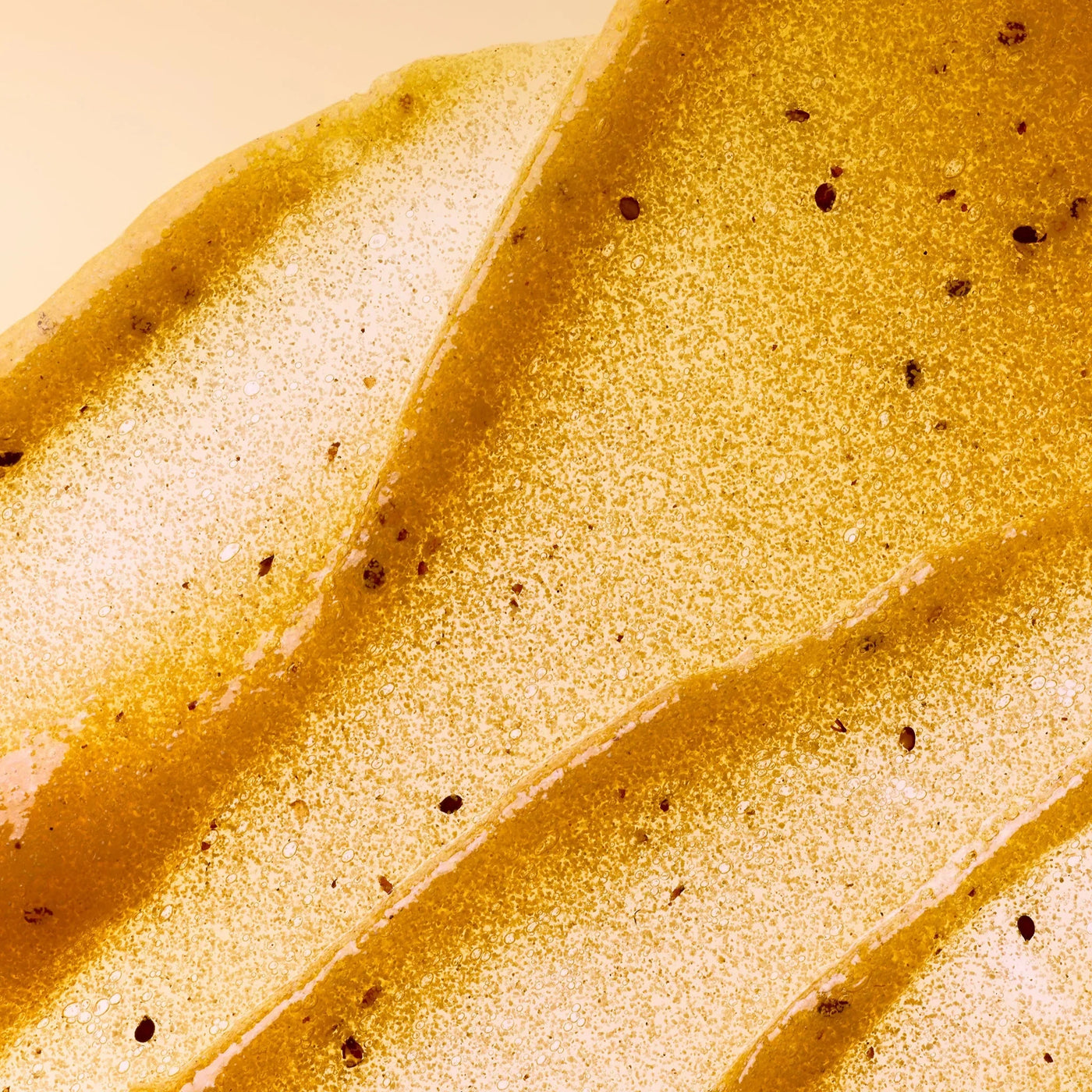 Close-up of Refreshing Passionfruit gel body scrub spread out on a surface with brown passionfruit seeds speckled throughout